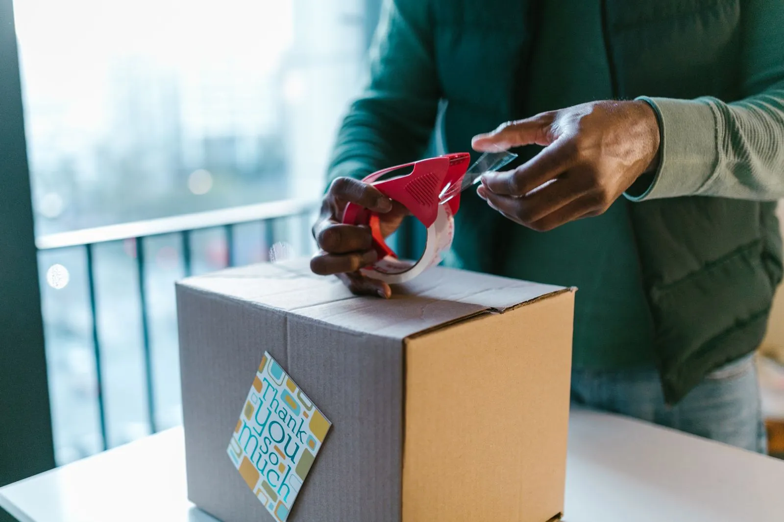 A business owner taping a parcel shut, a thank-you card already stuck to the box