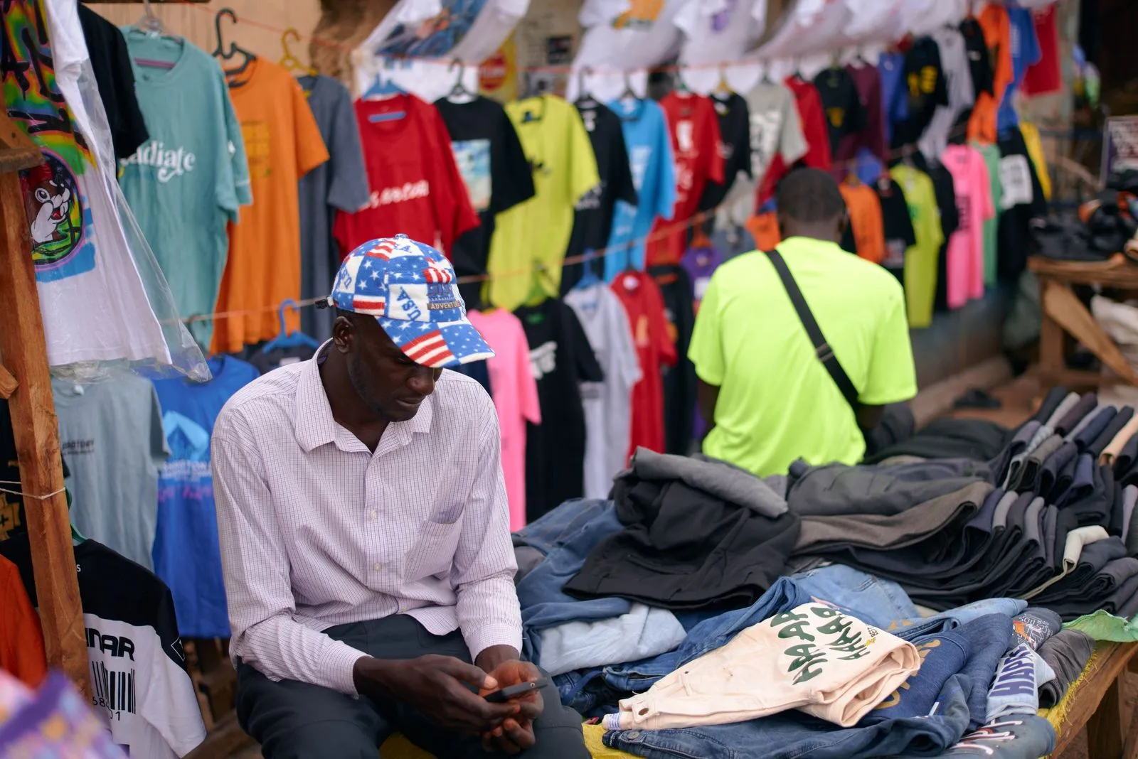 A clothing seller checking his phone at his stall in a market in Jos, Nigeria