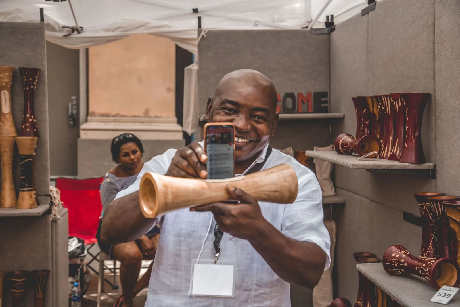 A maker in his market stall smiling as he photographs one of his handmade wooden pieces with his phone